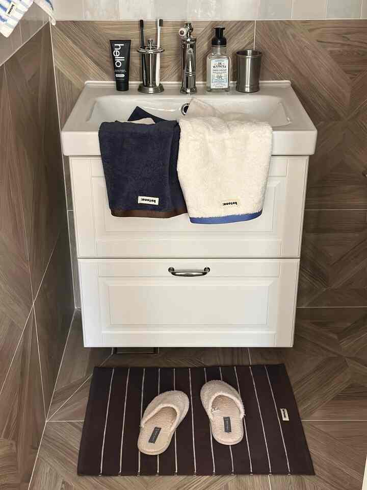 ホワイトとブラウンの色調のバスルーム、清潔な洗面台とタオル、バススリッパが配置された落ち着いた空間