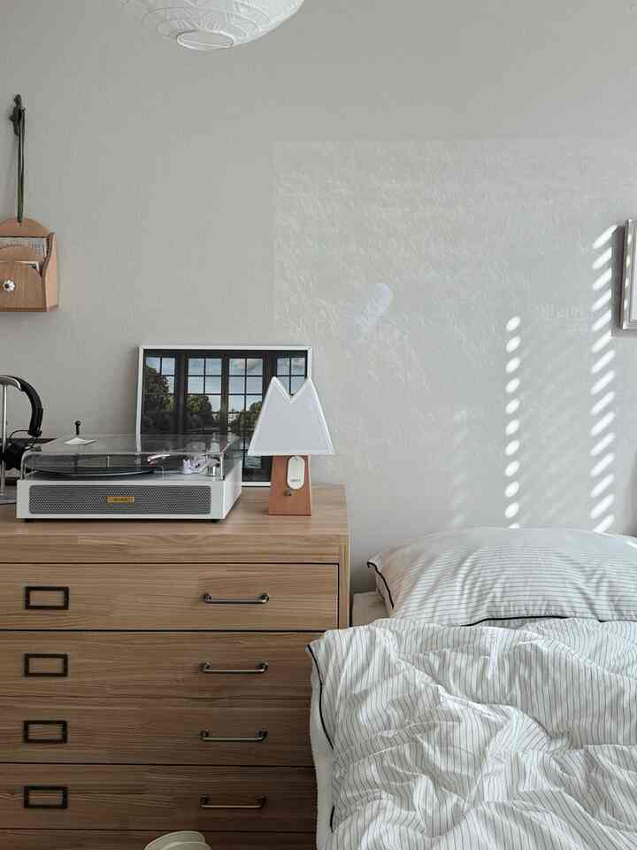 ナチュラルトーンの寝室、木製チェストと白のストライプ寝具が配置された落ち着いたインテリア