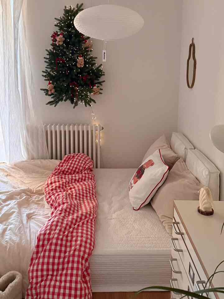 ホワイトとレッドのトーンが特徴的な寝室、クリスマスツリーの飾りとミニマルな家具が配置された雰囲気のあるインテリア