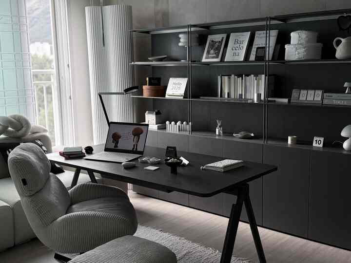 モノトーンとブラックを基調としたリビング書斎、黒の本棚と作業用デスク、グレーのリクライニングチェアが配置された洗練された雰囲気のあるインテリア