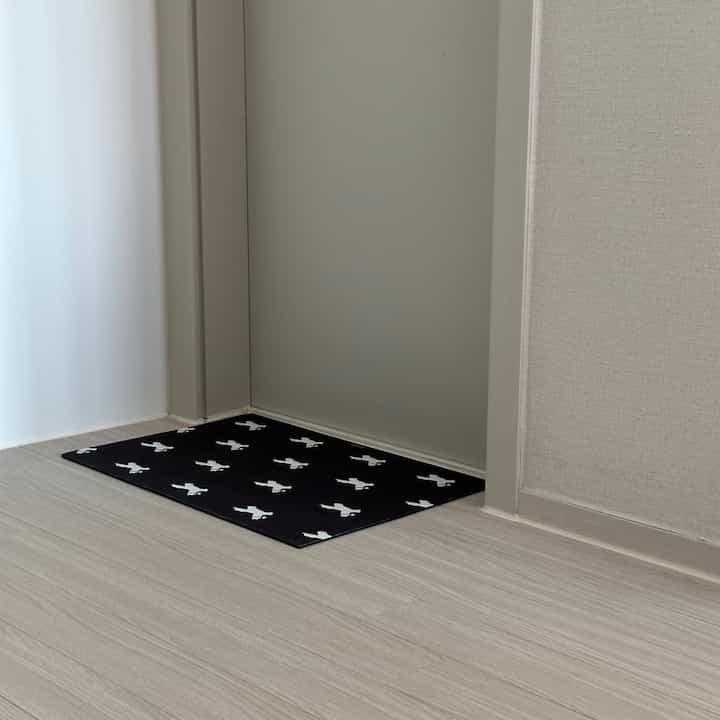落ち着いたベージュの床と壁の玄関、かわいい馬の柄がある黒いバスマットが置かれた清潔感のある空間