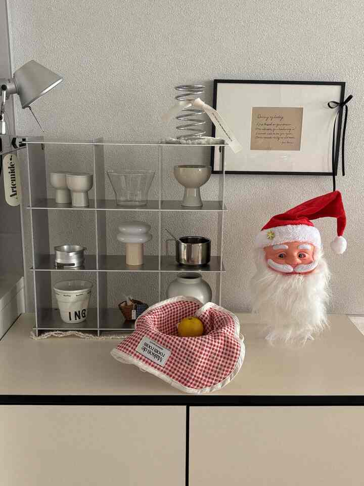 白と銀色のトーンのキッチンスペース、整理された棚と額縁、サンタの飾りとチェック柄のテーブルランナーが配置されたミニマルな雰囲気のインテリア