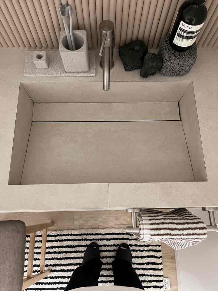 ベージュとグレーのトーンの乾式洗面台空間、珪藻土の歯ブラシホルダーとトレイが配置されたミニマルな雰囲気のあるトイレインテリア