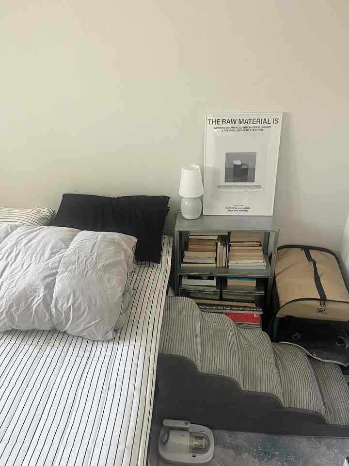 白い壁とグレーの寝具を備えた寝室、ベッド横に金属製の棚とペット用の階段が配置された落ち着いた空間