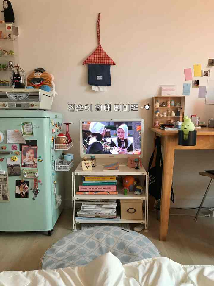 ミント色のレトロな雰囲気の小さなリビング、テレビ、ミニ冷蔵庫、デスク、フロアクッションが配置された落ち着いた空間
