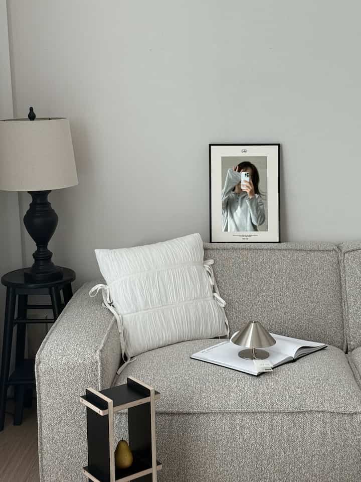 ナチュラルカラーのリビング、モダンなソファと鏡、テーブルランプが配置された印象的な空間