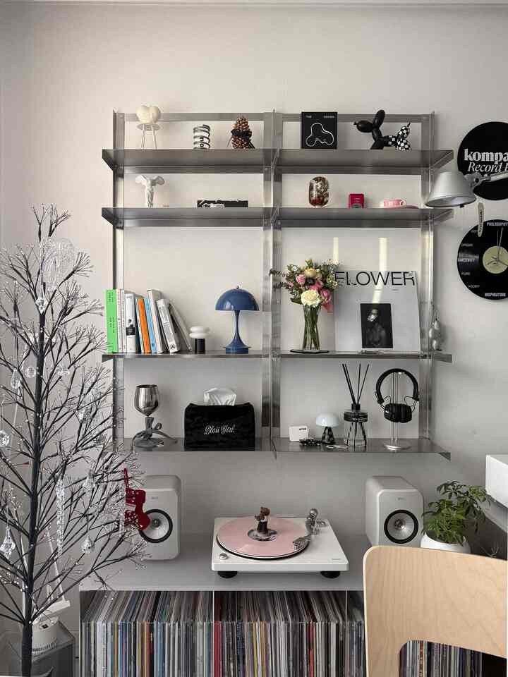 モダンな金属製の棚とヴィンテージターンテーブル、花瓶や照明が配置された雰囲気のある音楽空間