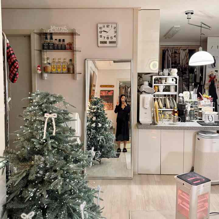 白とナチュラルカラーのキッチンとリビング、クリスマスツリーと大型鏡が配置された雰囲気のあるインテリア