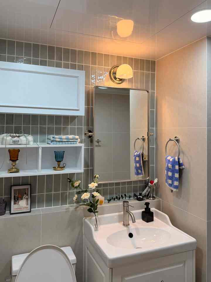 白とグレーのトーンのバスルーム、洗面台と鏡、壁付け照明が配置された清潔感のあるインテリア