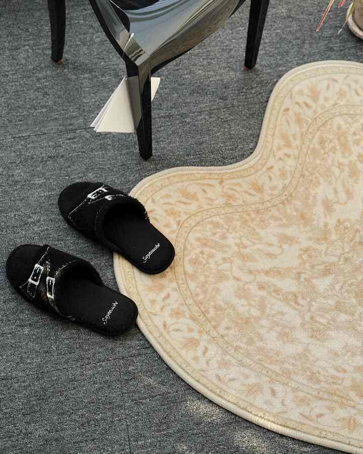 Close-up of beige patterned rug and black slippers on gray carpeted floor area