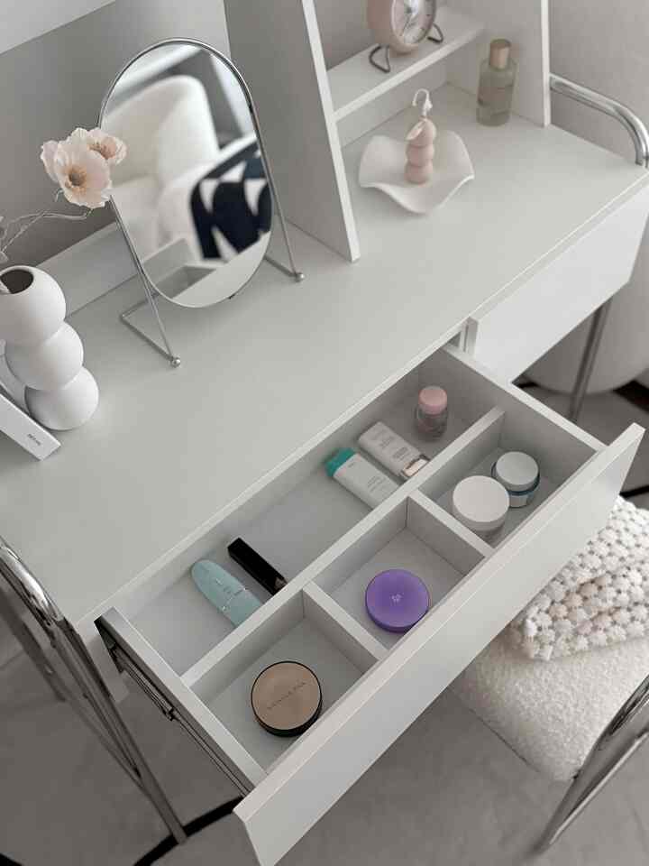 White and silver toned vanity table with an open drawer neatly organized with cosmetics in a simple modern space