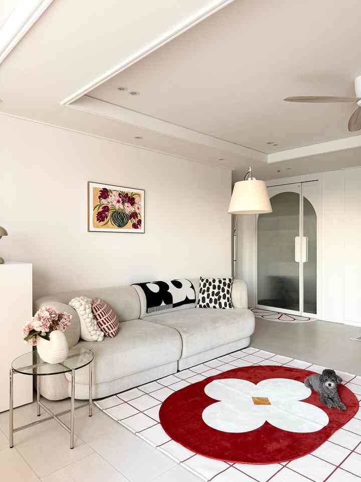 白と赤のトーンのリビング、ベージュのソファと赤い模様のラグ、小さな犬がいる清潔なミニマルスタイルの空間