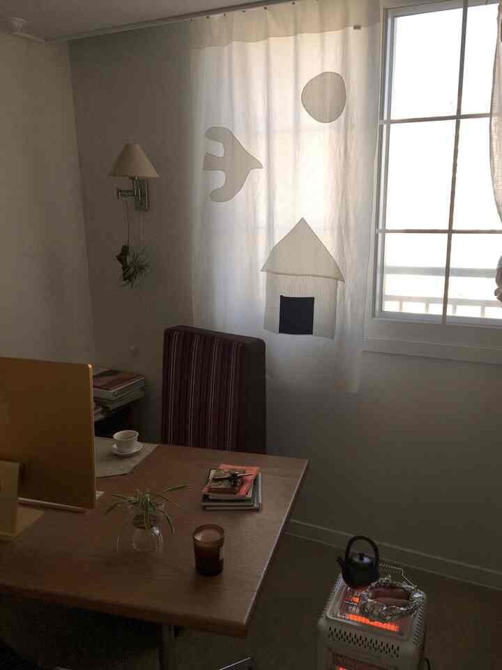 白い壁と木目調デスクが配置された狭いホームオフィス、自然な雰囲気の照明がポイントのインテリア