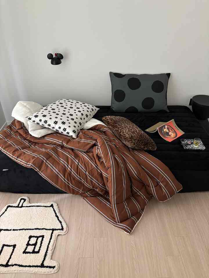 Single bedroom dominated by brown and black tones, featuring striped bedding and assorted pillows with a natural atmosphere