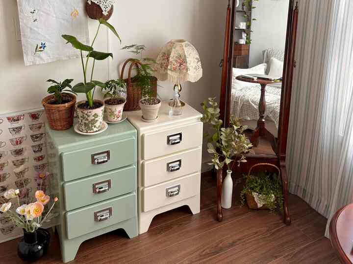 ナチュラルな色調のリビング、ベージュとグリーンの収納キャビネットに植物とヴィンテージのテーブルランプが配置された雰囲気のある空間