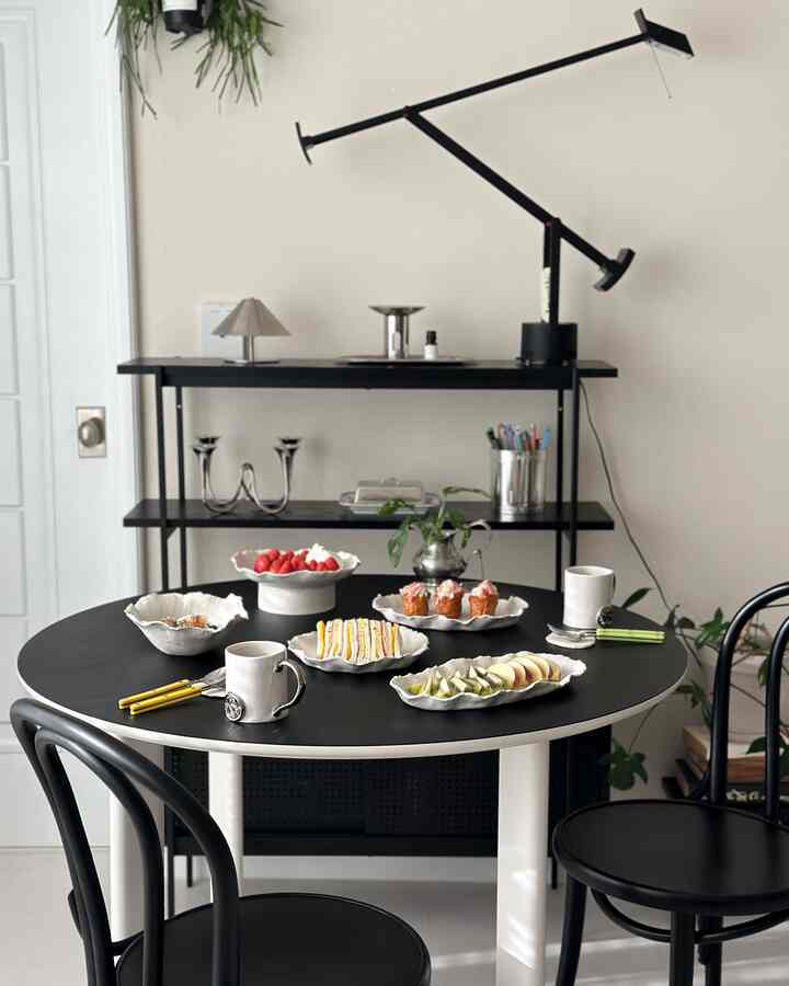 明るい色調のダイニングスペースに黒い円形テーブルと椅子が配置され、レザーのランチョンマットと簡単なデザートが置かれた雰囲気のあるインテリア