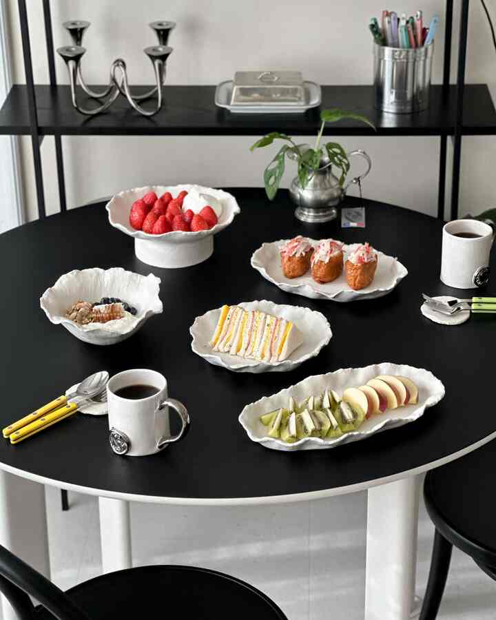 黒と白を基調としたダイニング、白い陶器の皿とマグカップが並ぶ黒い丸テーブルと椅子が配置されたモダンな空間