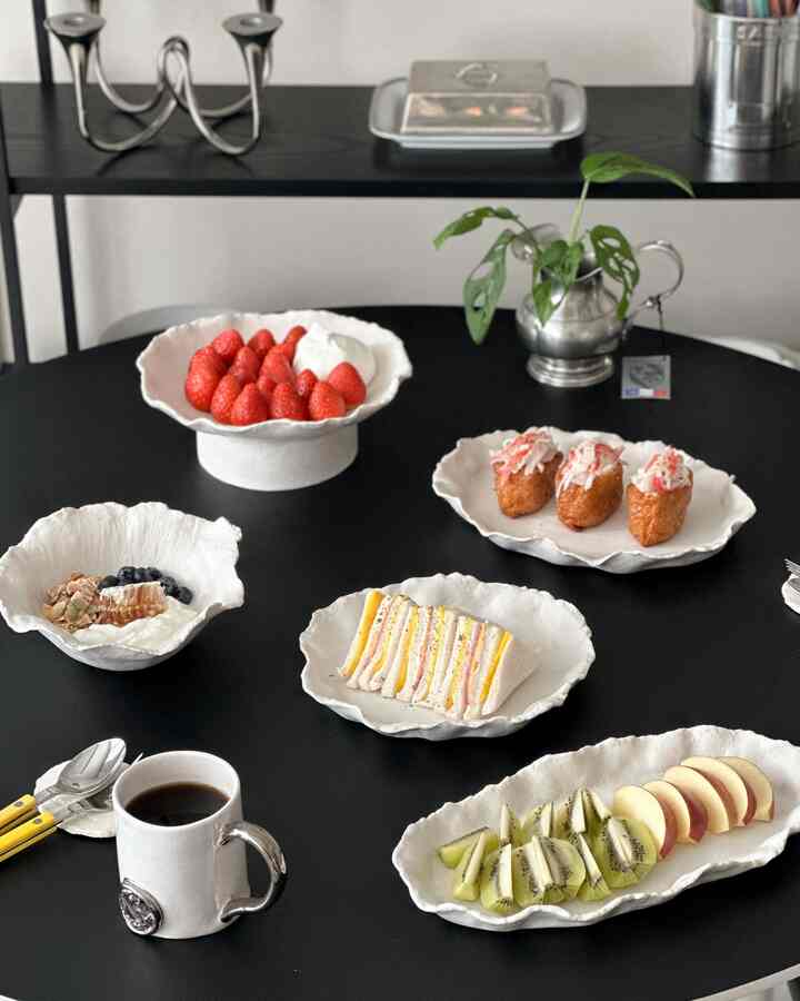 黒いダイニングテーブルに白い陶器の皿が並び、果物や料理が配置されたシンプルモダンなダイニング