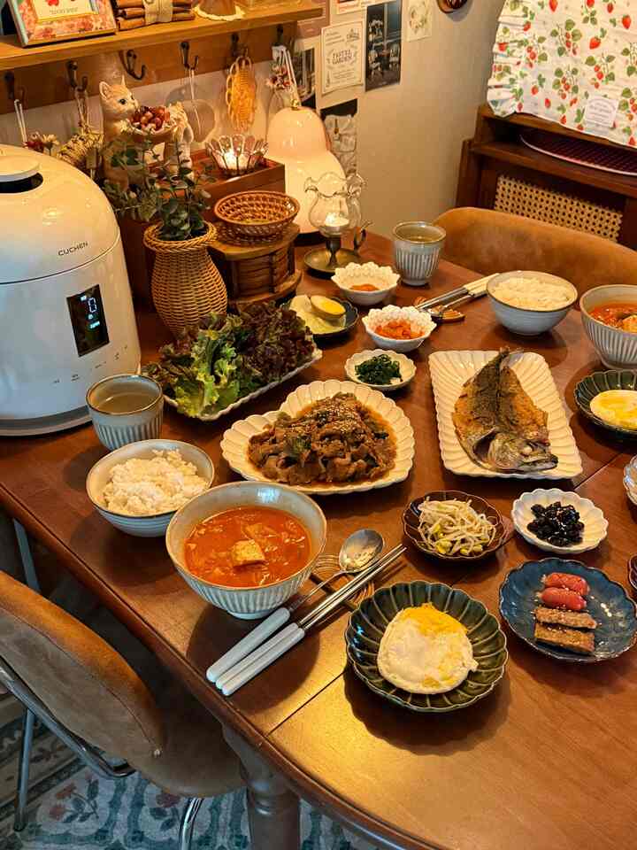 ナチュラルな木目調のダイニングルーム、テーブルの上に多様な韓国料理が丁寧に並べられた印象的な空間