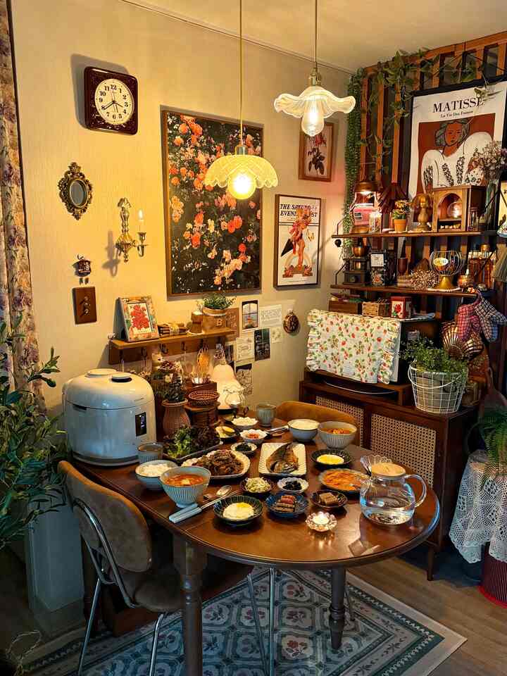 ベージュの壁とブラウンの木製家具が調和するヴィンテージ風のダイニングルーム、食卓に多彩な食器や植物が配置された雰囲気のある空間