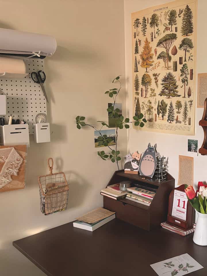温かみのあるベージュ色の壁にポスターと植物が配された、整理されたダークウッドのデスク空間