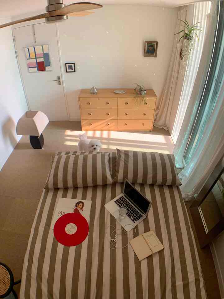 白とベージュの色調の寝室、ストライプの寝具と木製キャビネットが配置された落ち着いた雰囲気のインテリア