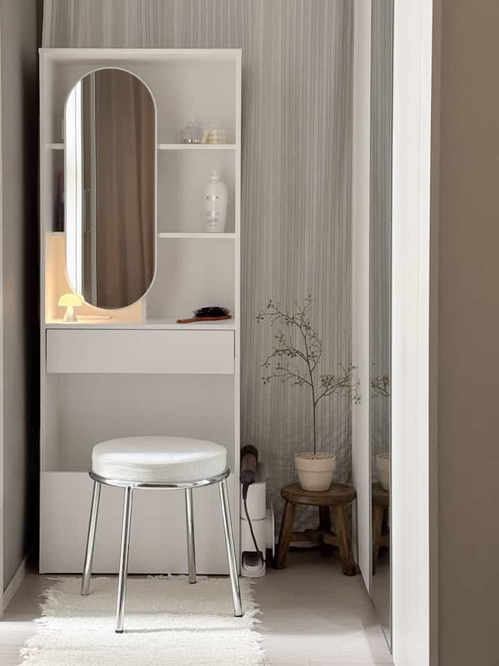 白とグレーのトーンでまとめられた小さな化粧台スペース、スツールと植物が配置されたモダンで自然な雰囲気のインテリア