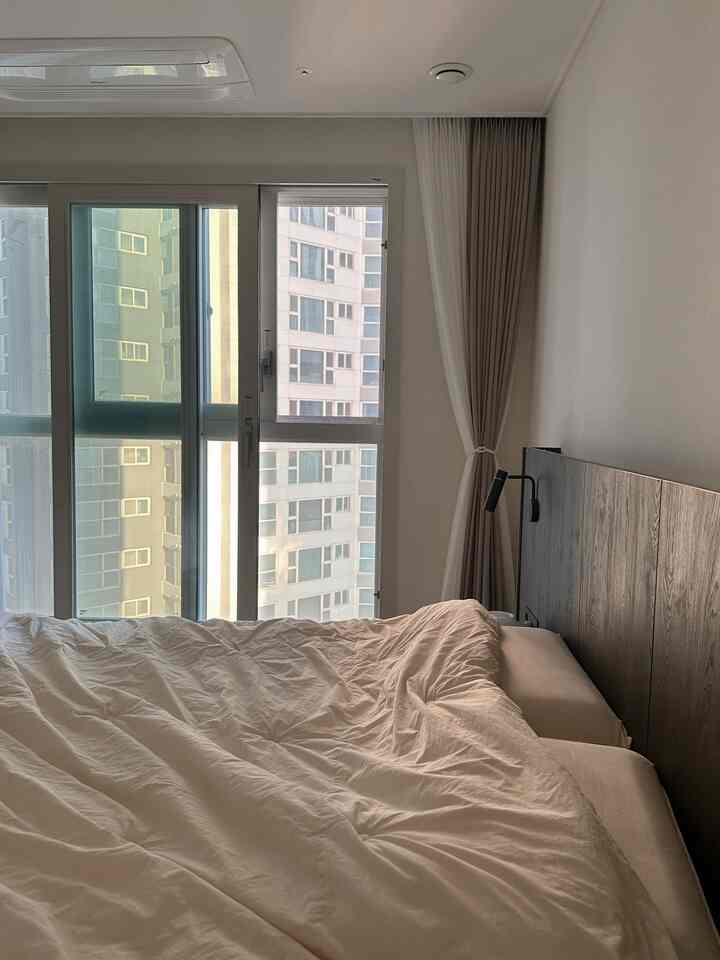 柔らかいベージュとホワイトトーンの寝室、大きな窓と木製のヘッドボードが配置された印象的な空間