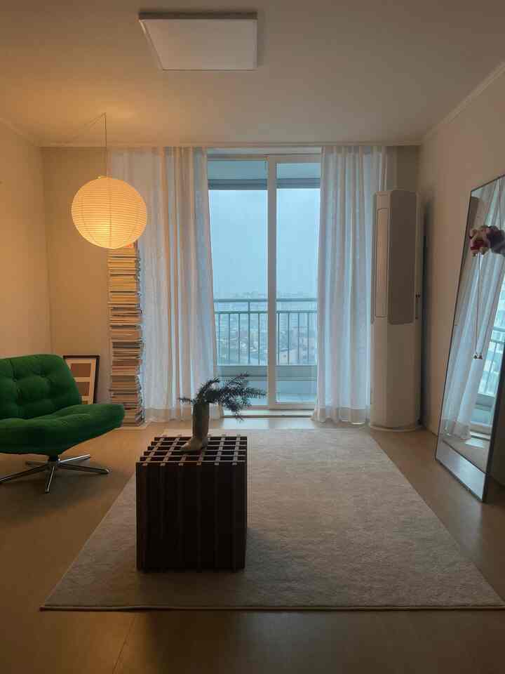 ナチュラルトーンのリビング、グリーンのアームチェアと棚、全身鏡が配置されたシンプルで居心地の良いインテリア