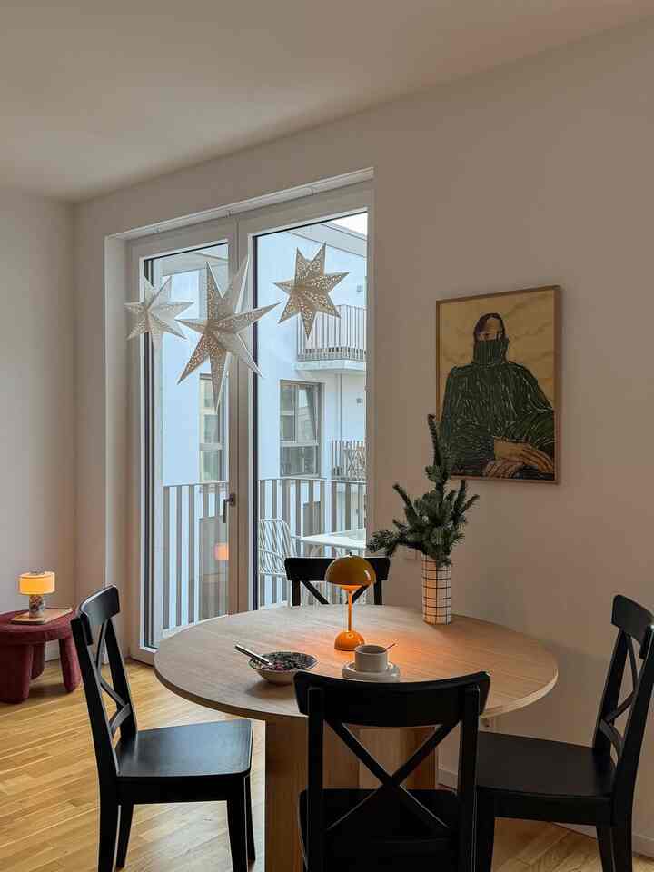 White walls and warm wood-tone dining room for four, featuring round table and black chairs, simple and cozy atmosphere