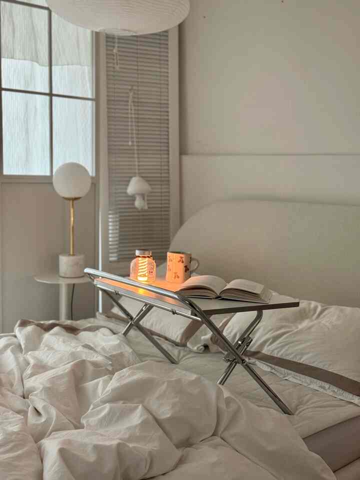 ベージュと白の色調の寝室、ベッドトレイに本とマッシュルームランプが置かれた雰囲気のあるインテリア