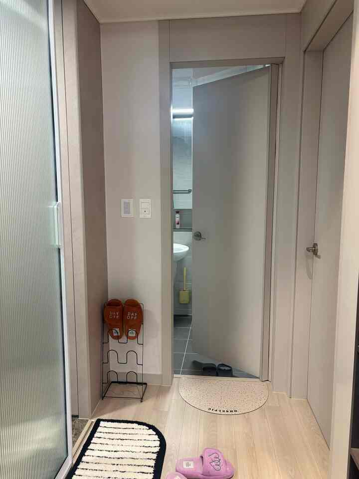 白と木目調の調和がとれたワンルームの玄関、シューズラックと厚めのバスマットが配置された雰囲気のある空間