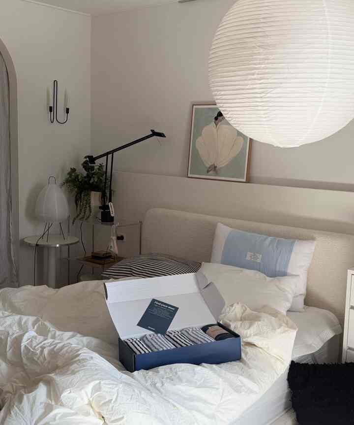 柔らかなベージュとホワイトの寝室、ポスターとテーブルランプが配置された雰囲気のあるインテリア