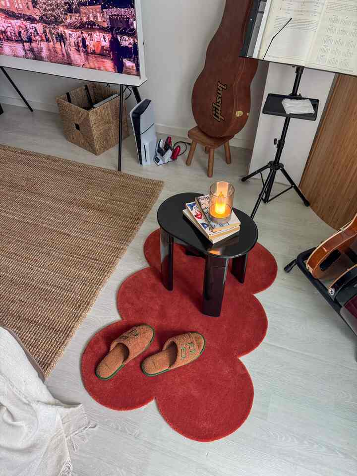 Cozy living and music space with red bath mat, brown woven rug, black coffee table, and guitar accessories arranged on light wooden flooring