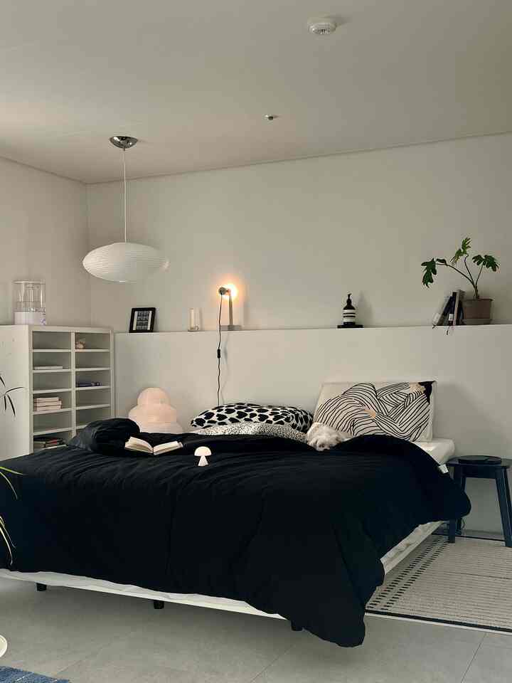 Modern bedroom in white and black tones featuring a bed with black bedding and simple lighting creating a cozy atmosphere