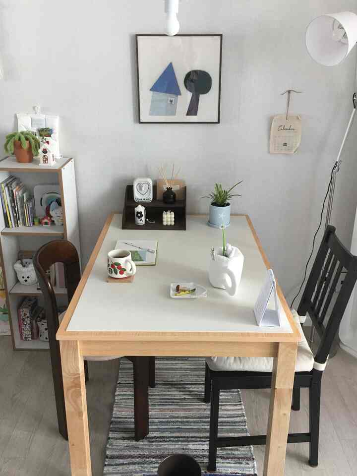 White walls and wood-tone dining table with two chairs in a small natural-feeling space for two-person household dining and reading