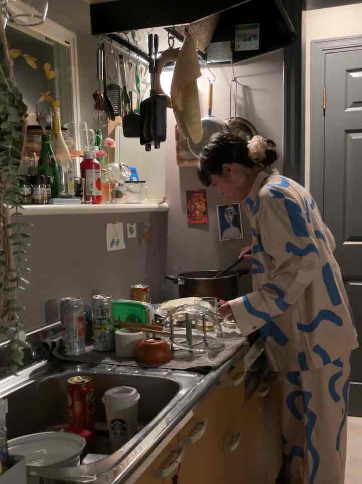 Cozy natural-toned small kitchen with a person cooking, featuring wooden cabinetry and blue patterned clothing blending harmoniously