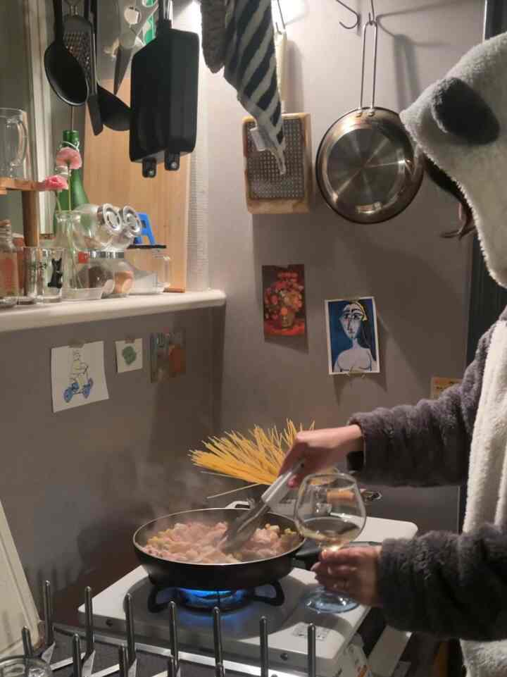 白とナチュラルのトーンの狭いキッチン、調理器具とガスレンジで料理をしている様子