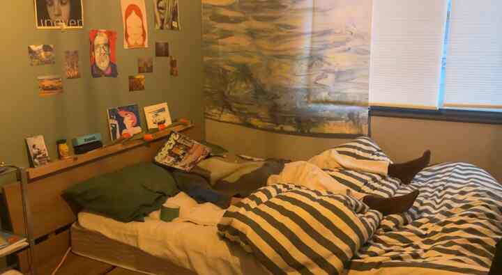 ナチュラルカラーの寝室、ストライプの掛け布団カバーと壁に飾られた複数のポスターがある雰囲気のあるインテリア