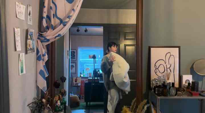 ベージュ色調の寝室兼ホームオフィス、緑のラグが印象的で、大きな鏡と収納が配置された雰囲気のあるインテリア