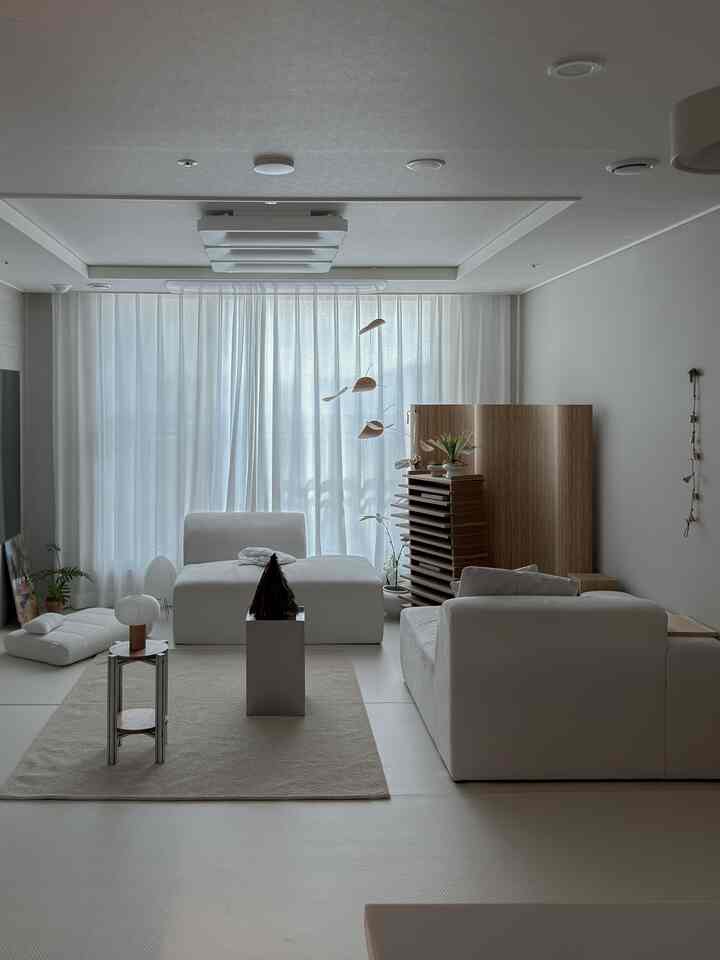 ホワイトとウッドトーンが調和したミニマルなリビング、モジュラーソファとラグが配置され、落ち着いた雰囲気のあるインテリア