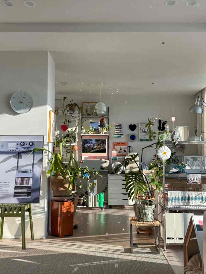 白い壁とナチュラルな木目調の床が印象的なリビング、数多くの植物と棚、ミニマルとマキシマルを融合させた雰囲気のあるインテリア