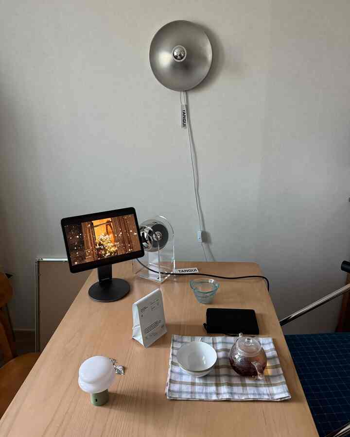 ナチュラルな色調のダイニングルーム、木製のダイニングテーブルと壁付け照明、テーブルランプ、ティーカップとタブレットが配置された雰囲気のあるインテリア