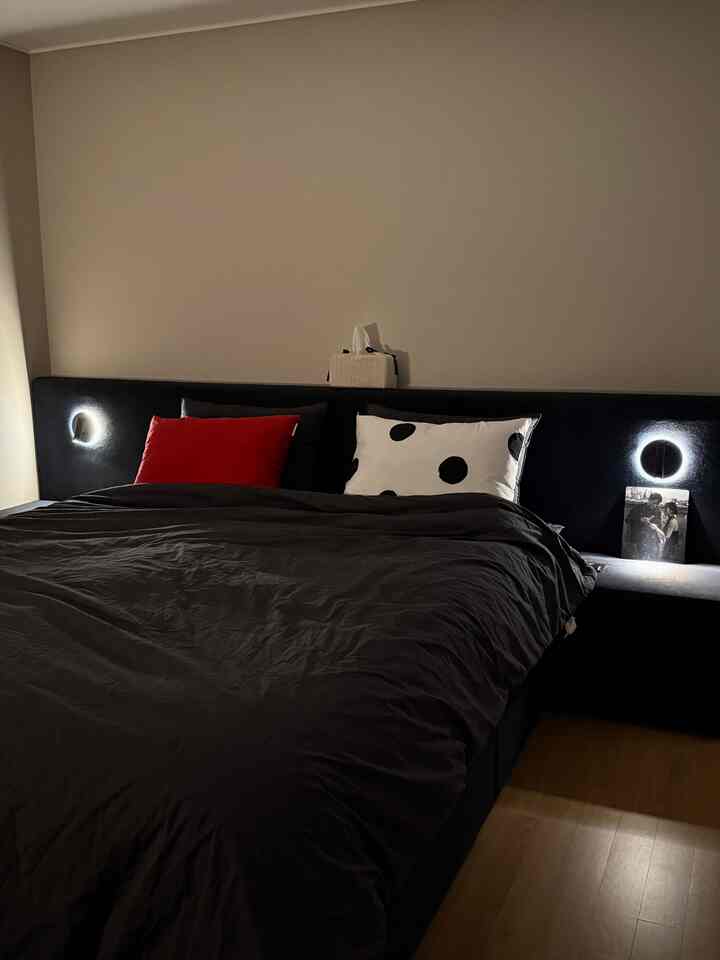 ダークネイビーのフレームベッドと黒い寝具が置かれた冬仕様の寝室、赤とドットのクッションがアクセントとなり落ち着いた暖かい夜の雰囲気を演出