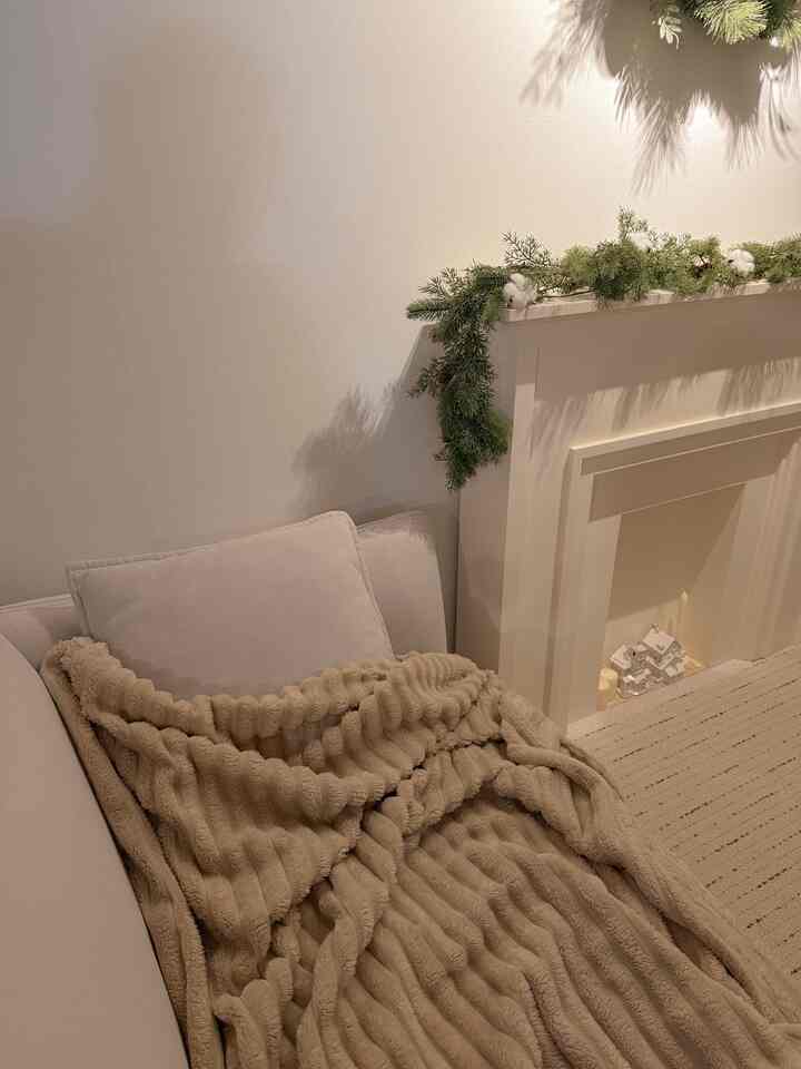 白とベージュの色調のリビング、ベージュのブランケットがかけられたソファとクリスマス飾りが配置された雰囲気のある冬のインテリア
