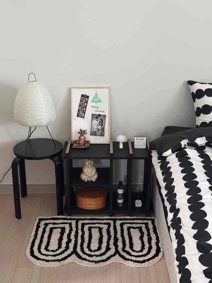 モノトーンの寝室、黒い本棚とパターン入りラグが調和する印象的な空間