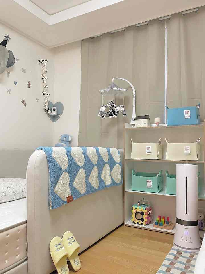 A beige and pastel blue toned baby room featuring a crib with throw blanket, hanging mobile, and neatly organized storage baskets creating a cozy atmosphere