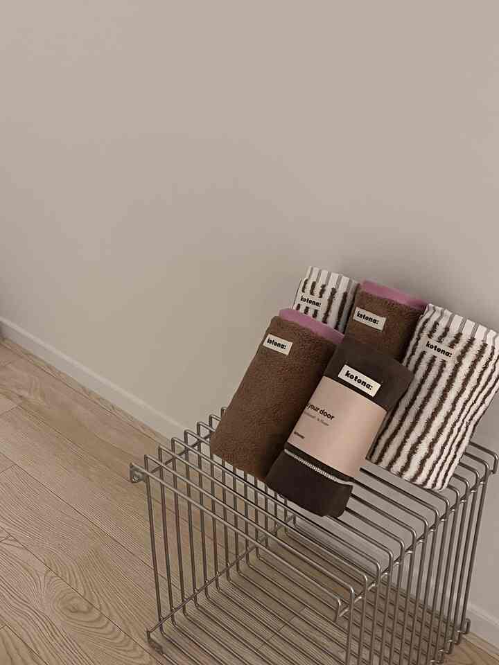 ナチュラルベージュとブラウンのタオルがワイヤーラックに整然と置かれた、シンプルで落ち着いたバスルームのインテリア