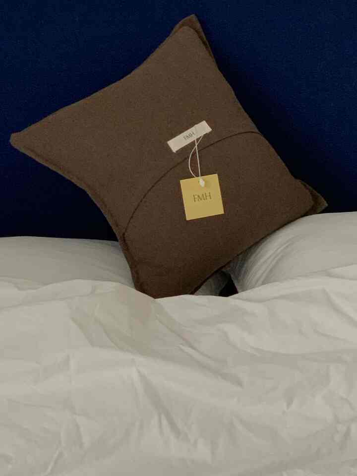 ネイビーブルーの壁を背景に、白い寝具と中央に配置されたブラウンクッションがあるシンプルな寝室のインテリア