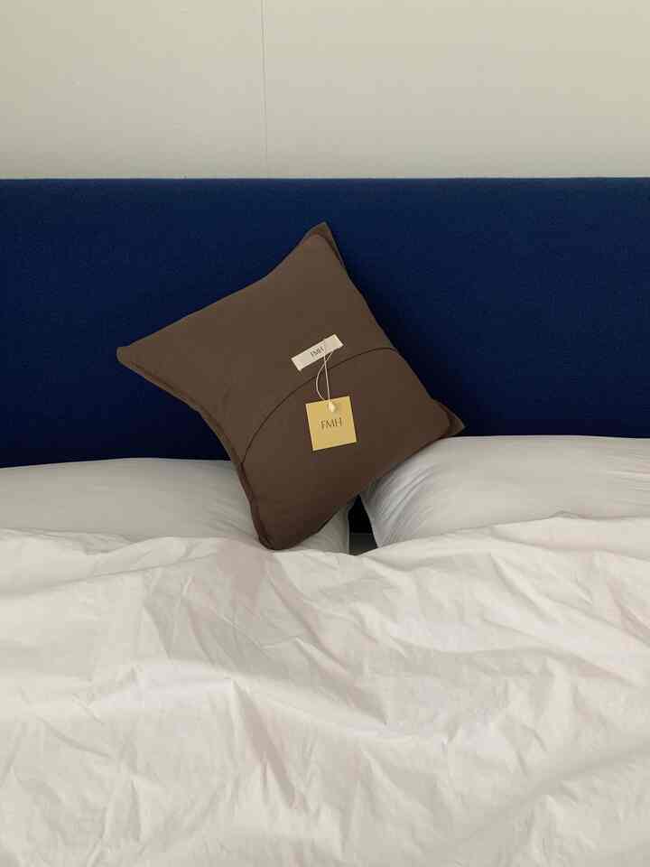 ネイビーカラーのヘッドボードとブラウンのクッション、ホワイトの寝具が配置された落ち着いた雰囲気の寝室